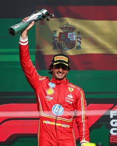 a man in a red racing suit holding up a green bottle on top of his head