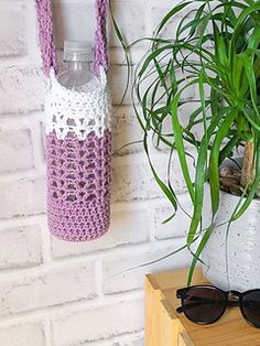 a potted plant next to a crocheted water bottle and sunglasses on a table