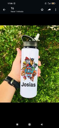 a hand holding a water bottle with the name josias on it in front of some bushes