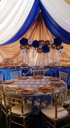 a banquet table set up with blue and white linens, gold plates and flower centerpieces