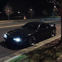 a black sports car parked on the side of the road at night with its lights on