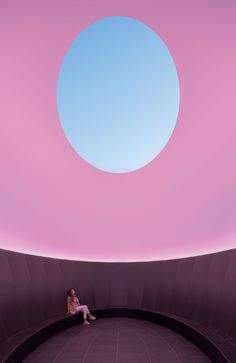 a person sitting on a bench in front of a pink wall with a blue sky