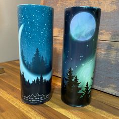 two tumbles sitting on top of a wooden table with trees and the moon painted on them