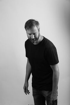 a man with a beard standing next to a suitcase and looking down at the ground