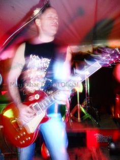 a man playing guitar in front of a red and white light with his head turned to the side