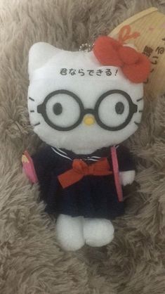 a hello kitty stuffed animal with glasses and a bow on it's head sitting on a furry surface