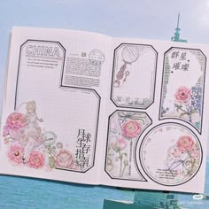 an open book with flowers and pictures on the pages, in front of a body of water