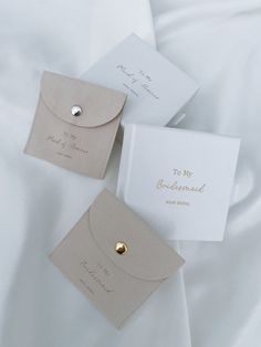 three wedding cards and envelopes laying on a white satin bed sheet with gold buttons