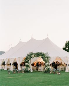 a large white tent set up with tables and chairs for an outdoor wedding reception in the grass