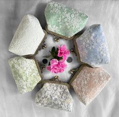 four different colored stones sitting on top of a white cloth covered surface with a pink flower in the middle