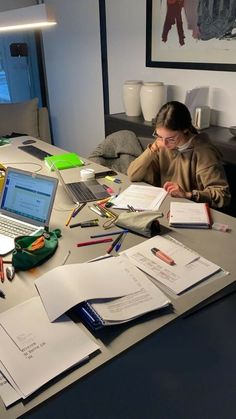 a person sitting at a desk with open books and laptop computer on top of it