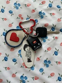 two keys are laying next to each other on a bed with flowers and heart shaped keychains