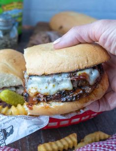 a hand is holding a sandwich with cheese and meat on it next to some crackers