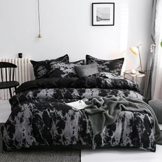 a bed with black and white comforters in a room next to a table, chairs and pictures on the wall