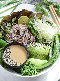 a plate with noodles, lettuce, and sauce on it next to chopsticks