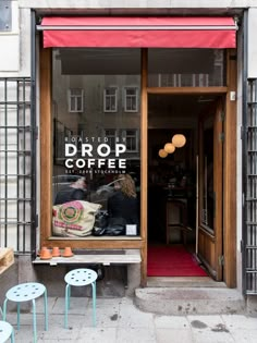 two people sitting on a bench in front of a coffee shop with red awnings