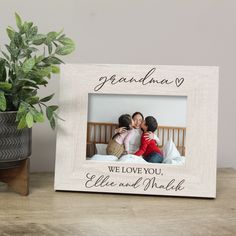 a wooden frame with the words grandma and two children on it, sitting next to a potted plant