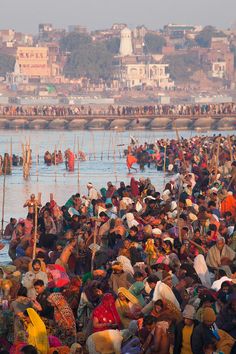 a large group of people standing in the water with boats and buildings in the background