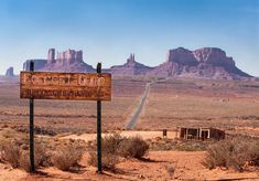 a wooden sign in the desert with mountains in the background