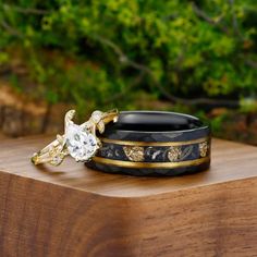 two wedding rings sitting on top of a wooden table in front of some green bushes