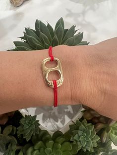 a woman's arm wearing a gold bracelet with a red cord and an initial charm