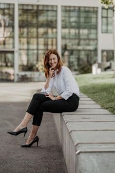 a woman is sitting on a wall talking on her cell phone and smiling at the camera