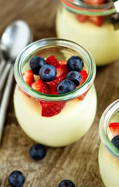 two jars filled with yogurt and fruit on top of a wooden table next to spoons