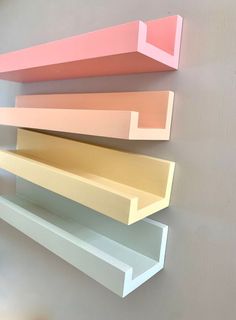 three shelves on the wall are painted different shades of pink, yellow and white with one shelf below them