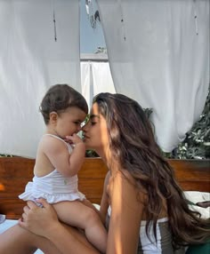 a woman holding a small child in her lap while sitting on a bed with white sheets