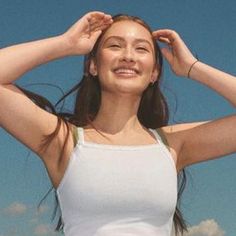 a woman is smiling and holding her hair in front of the camera while wearing a white tank top