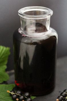 a glass jar filled with black berries next to leaves