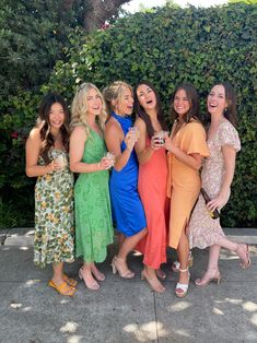 a group of women standing next to each other in front of a green wall and bushes