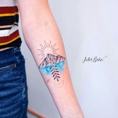 a woman with a tattoo on her arm and mountains in the background is wearing a striped shirt