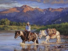 two men riding horses across a river with mountains in the background