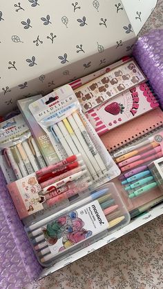 an open box filled with lots of different types of pens and pencils on top of a bed