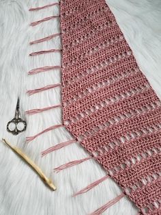 a pink crocheted tie next to a pair of scissors on a white furnishing