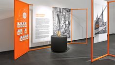 an orange and white display in a room with pictures on the wall, two black pedestals