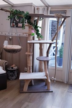 a cat tree in a living room next to a chair and table with plants on it