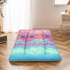 a colorful futon mattress sitting on top of a wooden floor next to a window