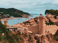 an old castle perched on top of a cliff next to the ocean with boats in the water