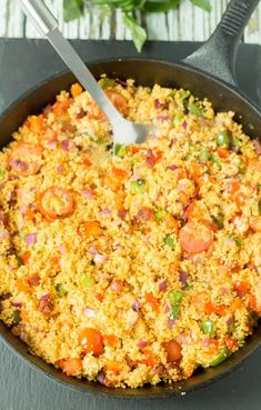 a skillet filled with rice and vegetables on top of a table next to a spoon