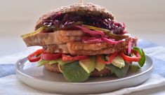 a sandwich with meat, lettuce and tomatoes on a white plate next to a blue towel