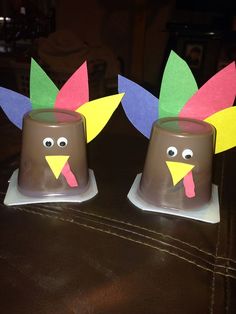 two plastic cups decorated like turkeys with paper decorations on the top and one has a fake turkey's head