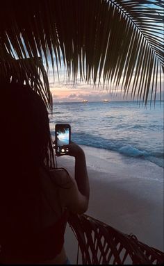 a woman taking a photo with her cell phone on the beach at sunset or dawn