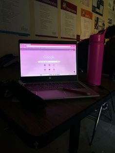 a laptop computer sitting on top of a wooden desk next to a pink trash can