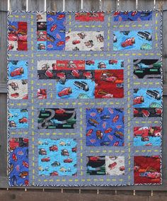 a quilt made to look like cars is hanging on a fence