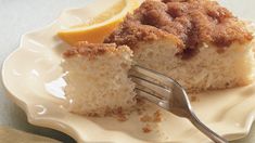 a piece of cake on a white plate with a fork and lemon wedged in it