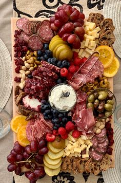 a platter filled with meat, cheese and fruit on top of a table cloth