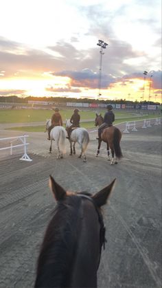 several people riding horses on a track at sunset