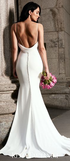 a woman in a white dress is holding flowers and looking down at the ground with her back to the camera